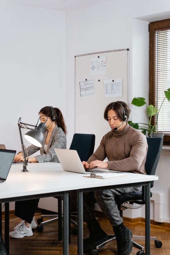 Deux collaborateurs avec casque et micro passent des appels depuis leur ordinateur portable dans un bureau