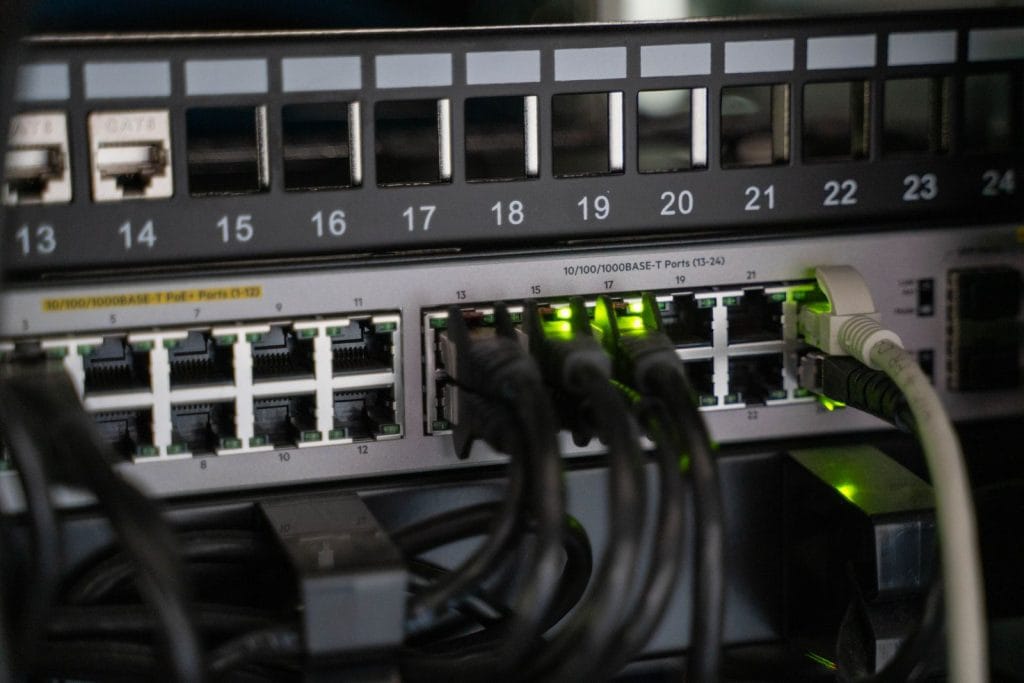 Switch réseau PoE dans une baie informatique, câbles Ethernet branchés et voyants verts allumés, sous un panneau de brassage